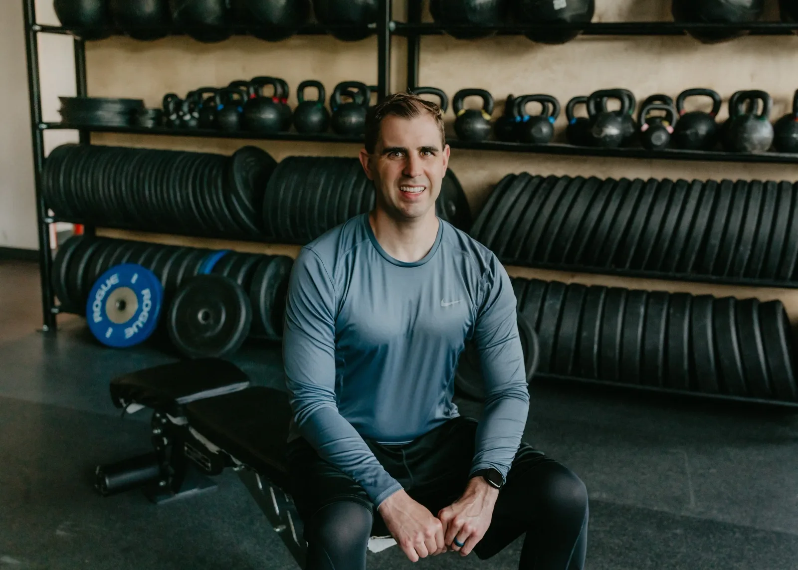 Nathan Brennan sitting on a weight bench in front of racks of kettlebells and plates