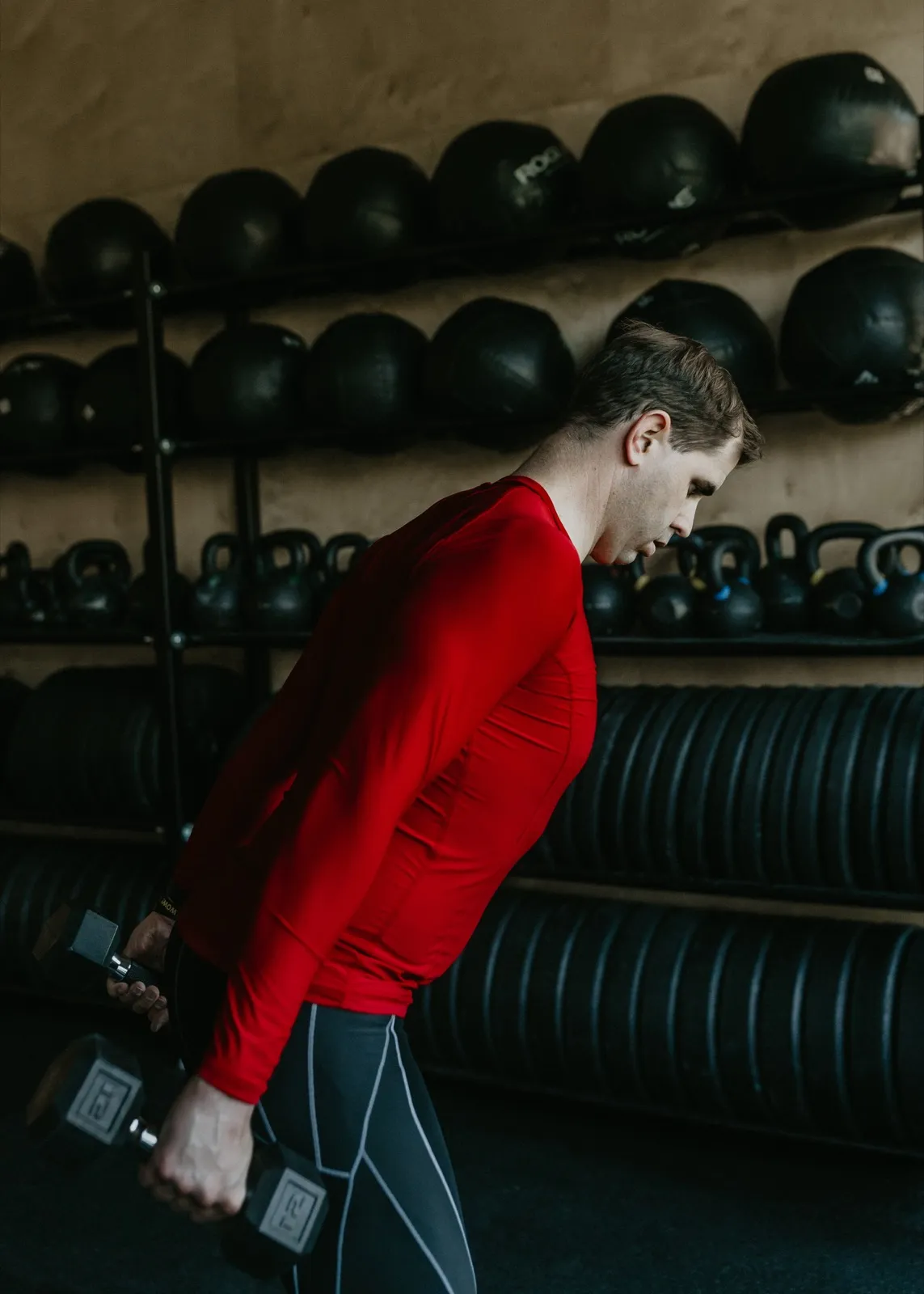 Nathan Brennan carrying dumbbells past a rack of slam balls