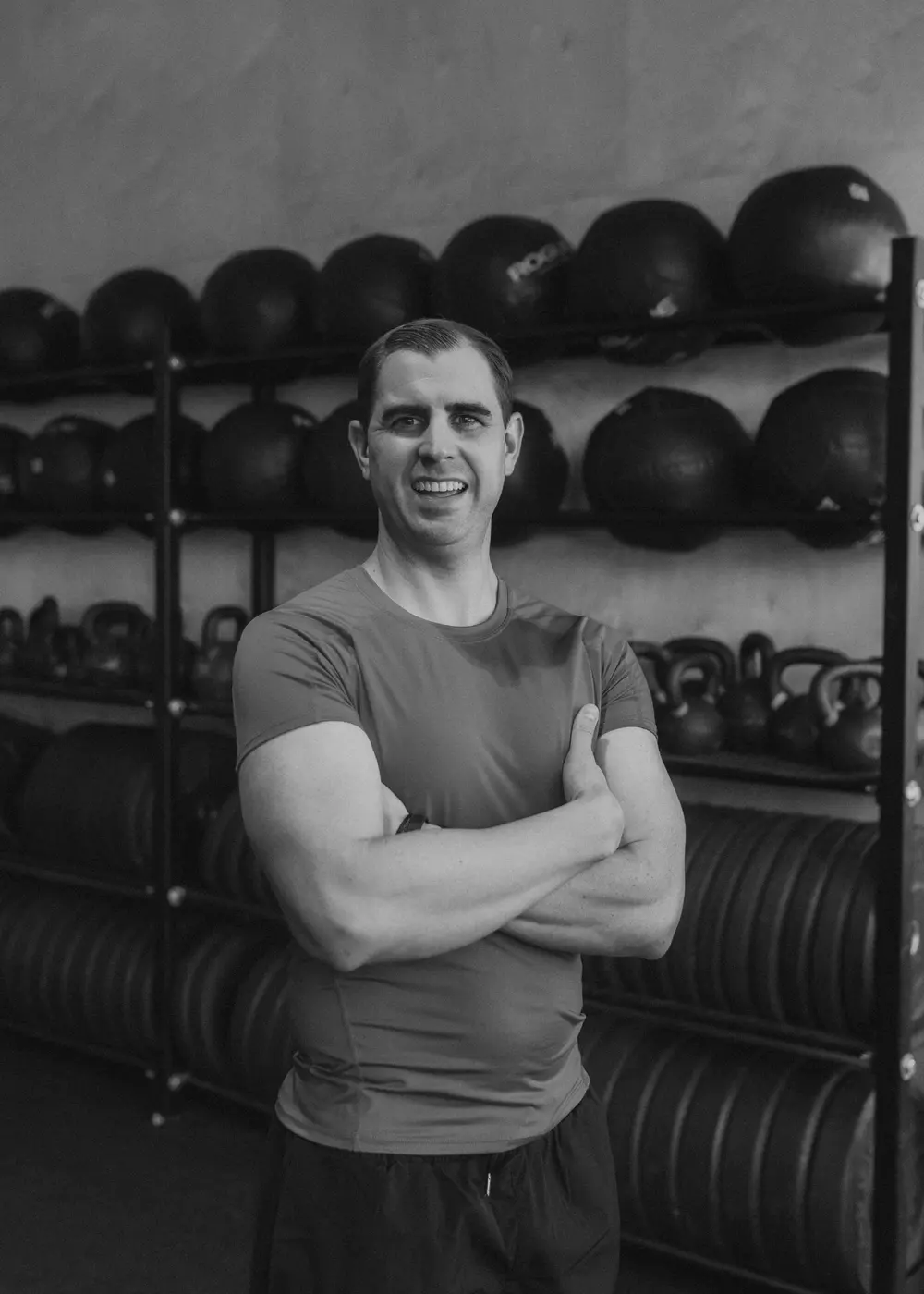 Nathan Brennan standing with his arms crossed in front of racks of medicine balls and kettlebells