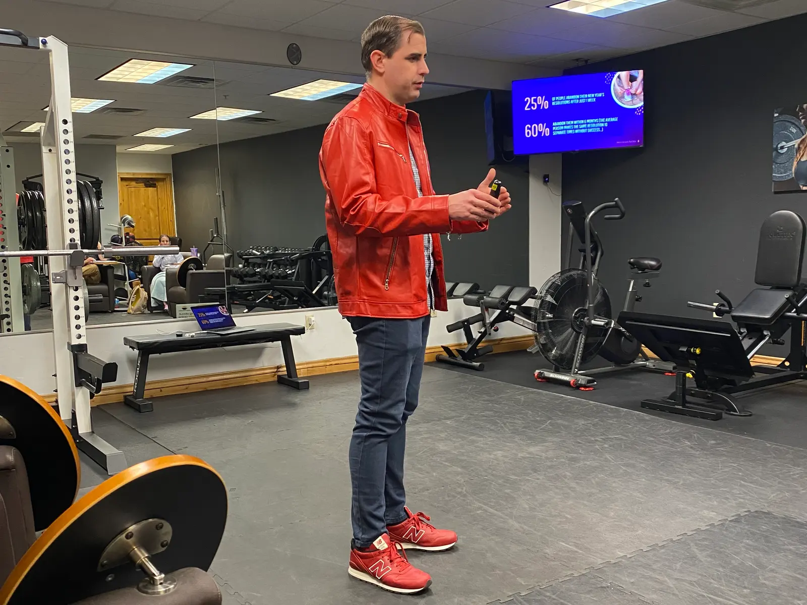 Nathan Brennan presenting a fitness seminar, gesturing beside a screen showing statistics on abandoned New Year's resolutions